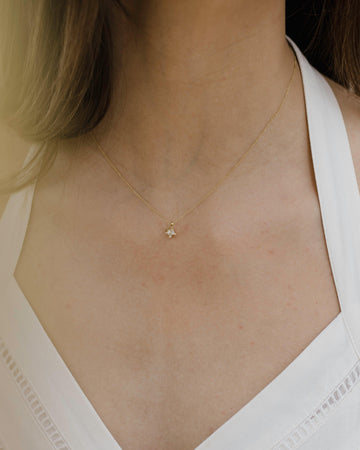 Γυναικείο χρυσό κολιέ με μονοπετράκι στο κέντρο στολισμένο με μικρά ζιργκόν περιμετρικά, φορεμένο σε μοντέλο.